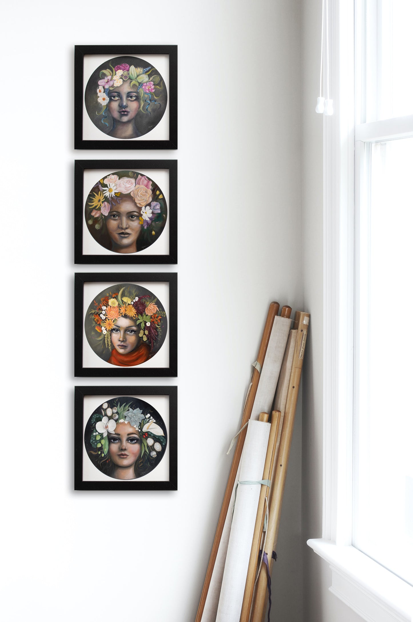 Instant gallery wall with set of 4 seasonal portrait prints. Each print features the flowers of Spring, Summer, Autumn/fall or Winter in their hair. Shown here framed in black on a white wall beside a bright window.